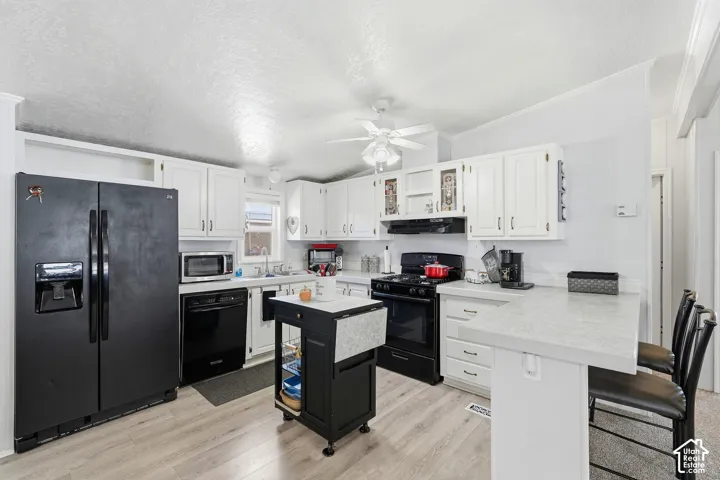 Kitchen featuring white cabinetry, light-toned countertops, black appliances, a ceiling fan, and wood-finish flooring