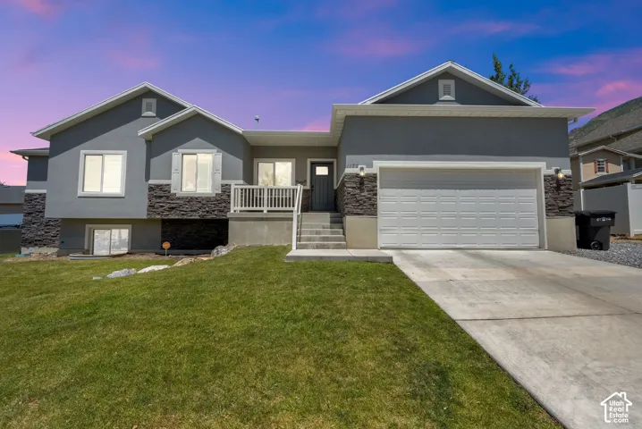 Stucco exterior with stone accents, attached two-car garage, concrete driveway, and front entryway with white railing