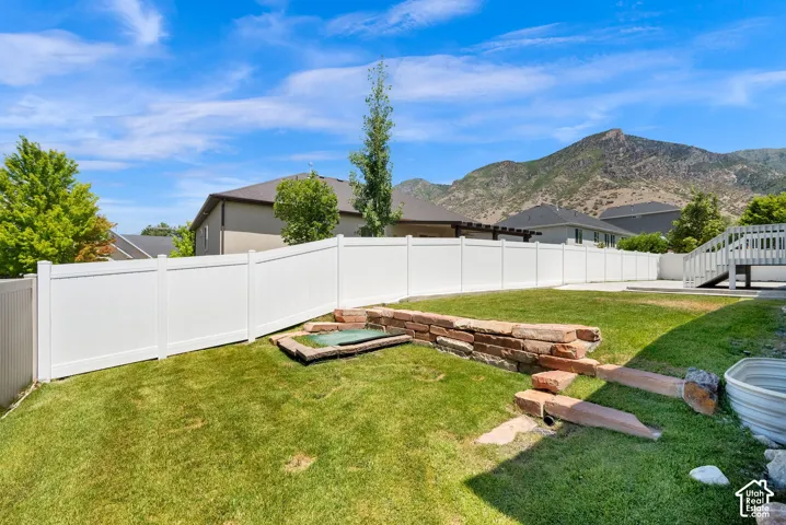 Expansive backyard featuring a white privacy fence, stone retaining wall, and a raised spa