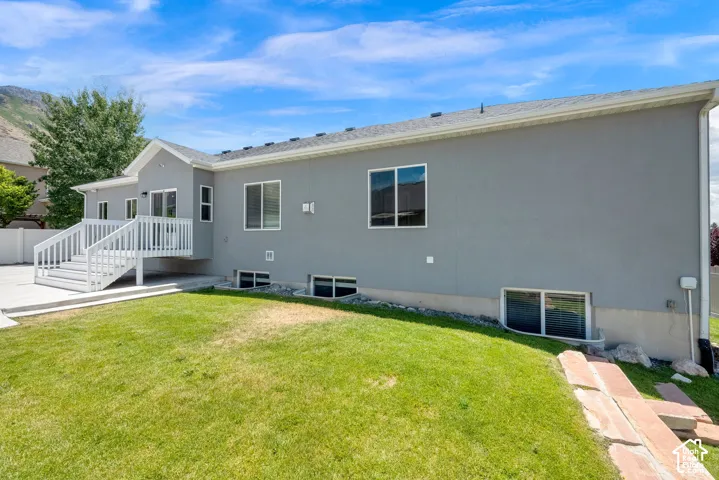 Expansive green lawn, concrete patio, white deck with railings, stucco exterior, and multiple windows