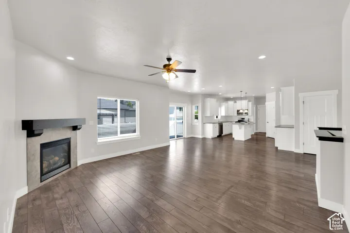 Open concept living area featuring wood-finish flooring, a corner fireplace with a dark mantel, a ceiling fan, and recessed lighting