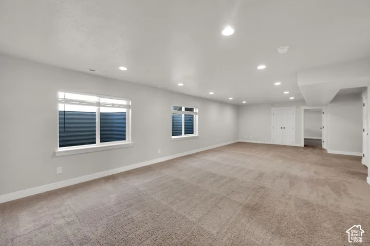 Spacious room featuring neutral carpeting, recessed lighting, double-door closet, and multiple windows