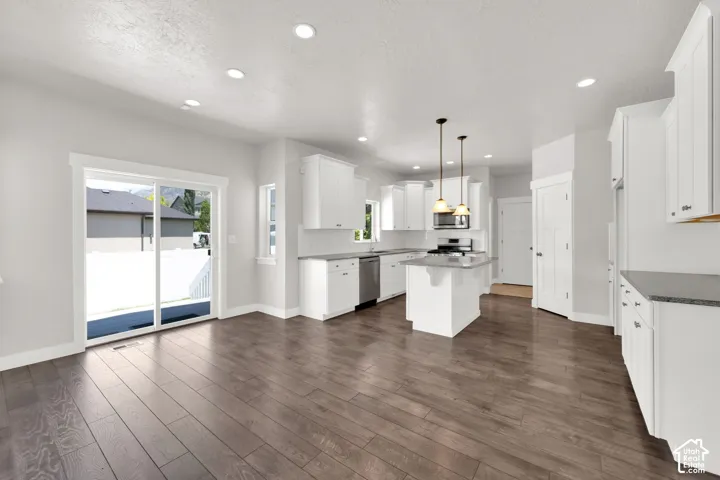 Open-concept kitchen with white cabinetry, stainless steel appliances, a kitchen island, pendant lighting, and wood-finish flooring