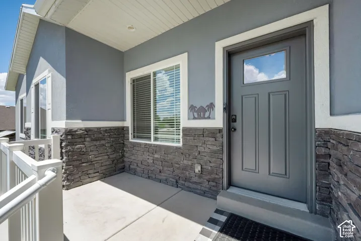 Covered entry porch featuring a paneled door with window, stone accent siding, and white railings