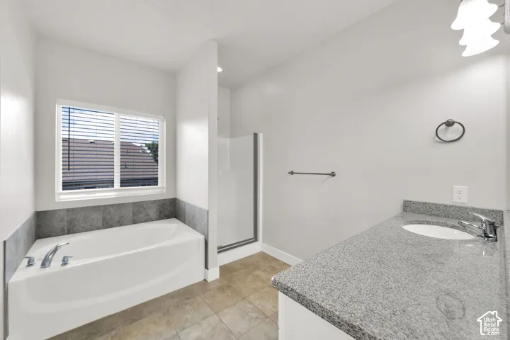 Spacious bathroom featuring a built-in tub, separate shower with glass enclosure, single vanity with light-colored countertop, and tiled flooring