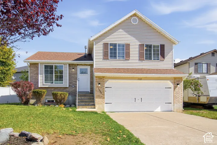 Split-level residence featuring a two-car garage, light-toned siding, and brick veneer accents