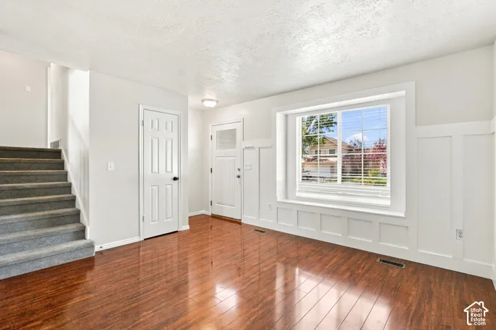Wood-finish flooring, staircase with carpeted treads, board and batten wall detailing, large window with blinds, and paneled doors