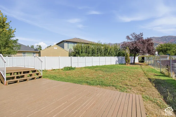 Expansive backyard featuring a wood-finish deck with white railings, a large grassy area, a white privacy fence, and mature trees