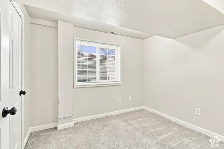 Room with light gray carpeting and white walls, featuring a white-framed window with blinds