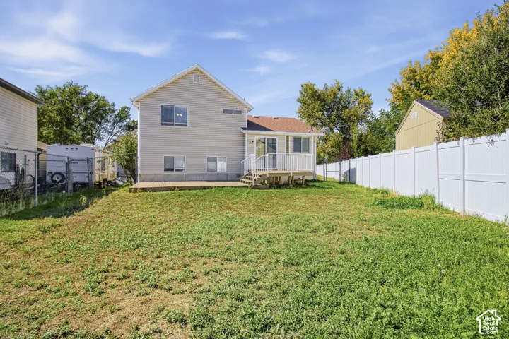 Expansive backyard featuring a deck with white railings, a patio area, and white privacy fencing