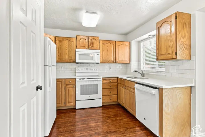 Kitchen featuring wood-finish cabinetry, white subway tile backsplash, white countertops, stainless steel sink, and wood-finish flooring