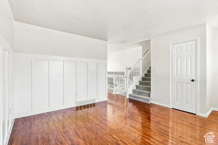 Wood-finish flooring, white paneled wall detailing, and a carpeted staircase with white railings