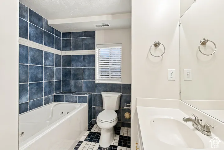 Built-in jetted tub surrounded by blue tile, checkered floor tile, single vanity with integrated sink, and brushed nickel fixtures