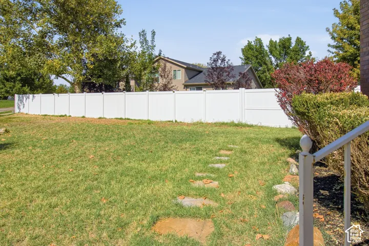 Expansive lawn area featuring a white privacy fence, stepping stone pathway, and mature landscaping