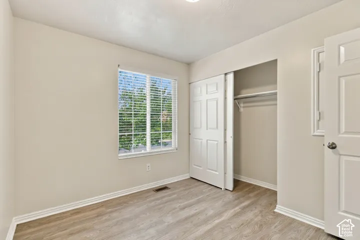 Neutral wall paint, wood-finish flooring, sliding closet doors, built-in closet rod, and window with blinds