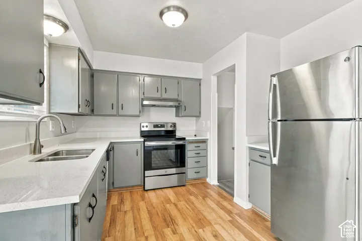 Kitchen featuring light gray cabinetry, light-toned countertops, wood-finish flooring, and stainless steel appliances