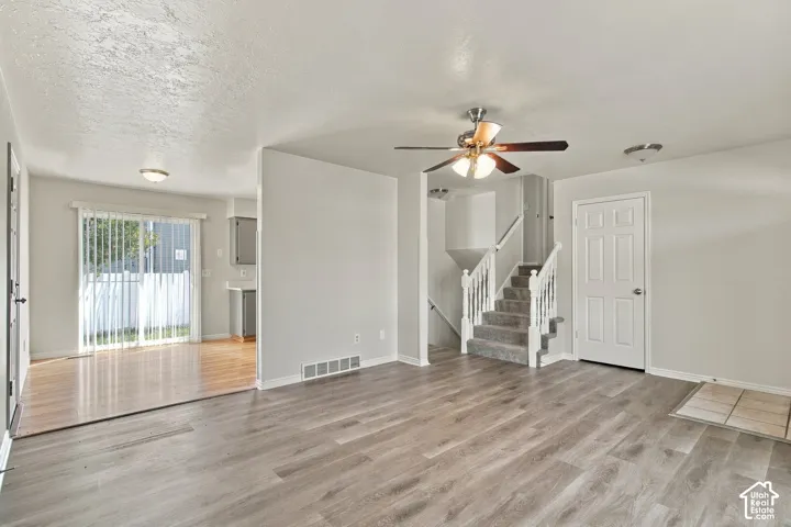 Laminate wood-finish flooring, central ceiling fan, and carpeted staircase with white railings