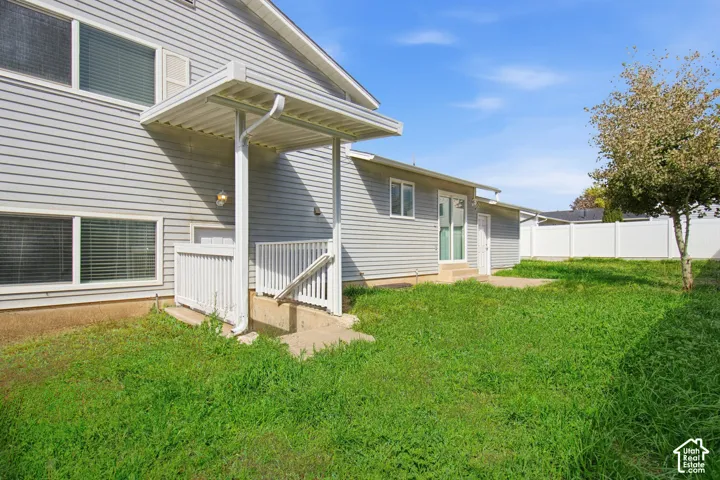 Vinyl siding exterior, covered patio, white railing, mature tree, and a white privacy fence