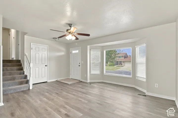 Wood-finish flooring, bay windows with blinds, ceiling fan with integrated lighting, paneled interior doors, and a carpeted staircase with white railing