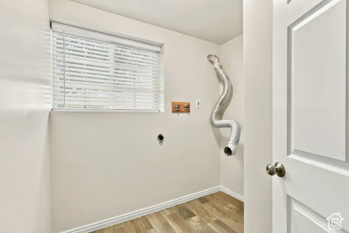 Laundry area featuring wood-finish flooring, a window with blinds, and a paneled door