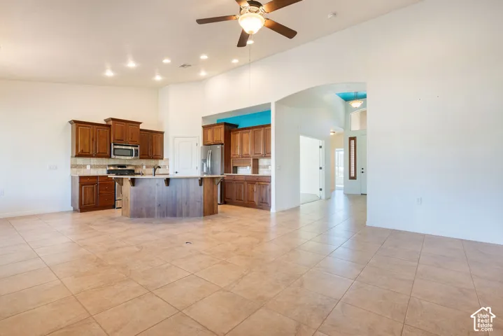 Spacious open-concept living area featuring tile flooring, vaulted ceilings, recessed lighting, and a ceiling fan