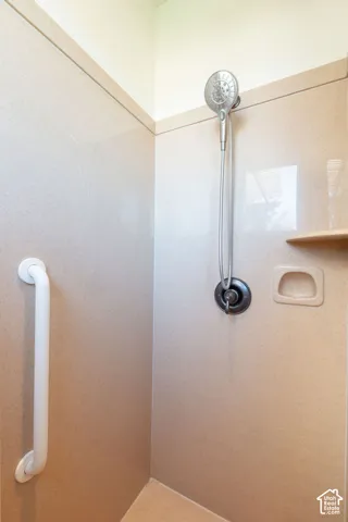 Shower stall with neutral-toned wall panels, a handheld showerhead, a built-in shelf, and an integrated grab bar