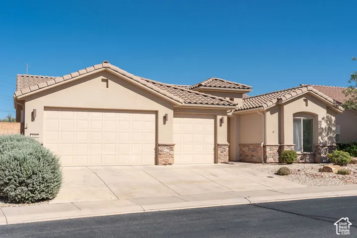 Stucco exterior with stone accents, concrete driveway, two garage doors, and a tiled roof