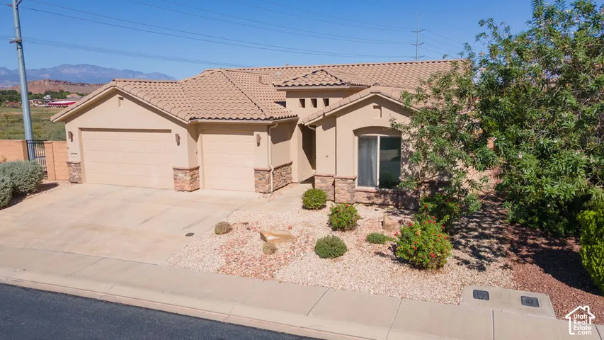 Stucco exterior featuring a tile roof, an integrated two-car garage, and a low-maintenance gravel landscape with shrubbery