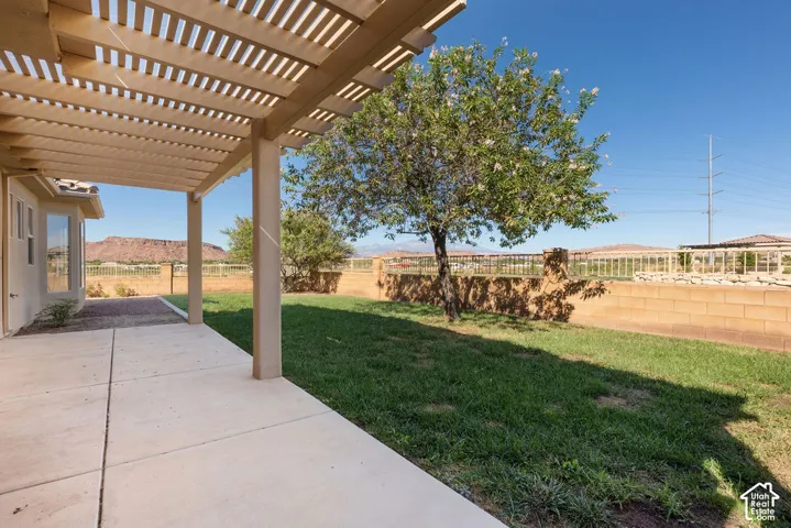 Patio with an attached pergola, providing access to a grassy yard with a block wall and distant mountainous scenery