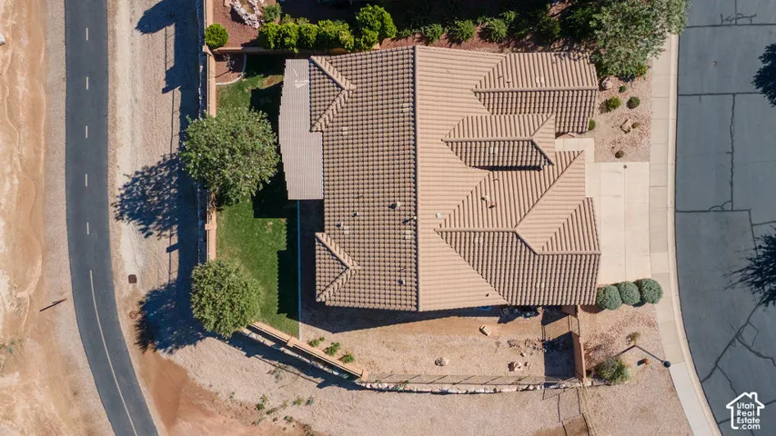 Pitched tile roof, concrete driveway, concrete sidewalks, landscaped front yard with shrubs and trees, and a partial grassed backyard