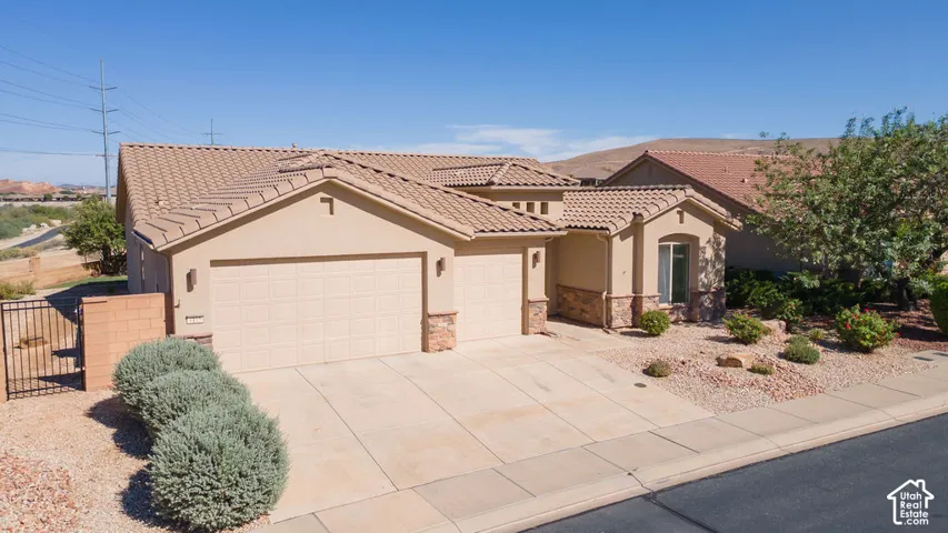 Stucco exterior with stone accents, tile roof, attached garage, paved driveway, and desert landscaping