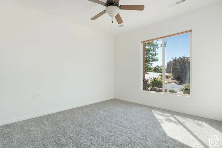 Light gray carpeting, white painted walls, a large window, and a ceiling fan with integrated lighting