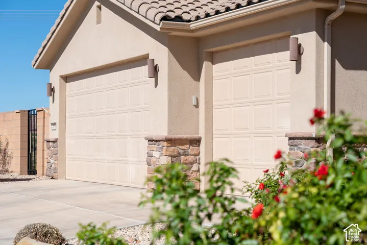 Stucco exterior featuring dual garage doors with panel detailing, stone accents, and wall-mounted exterior lighting