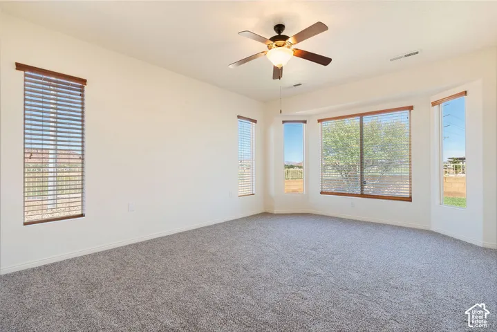Bay window with multiple panels, ceiling fan with integrated lighting, and neutral carpet flooring