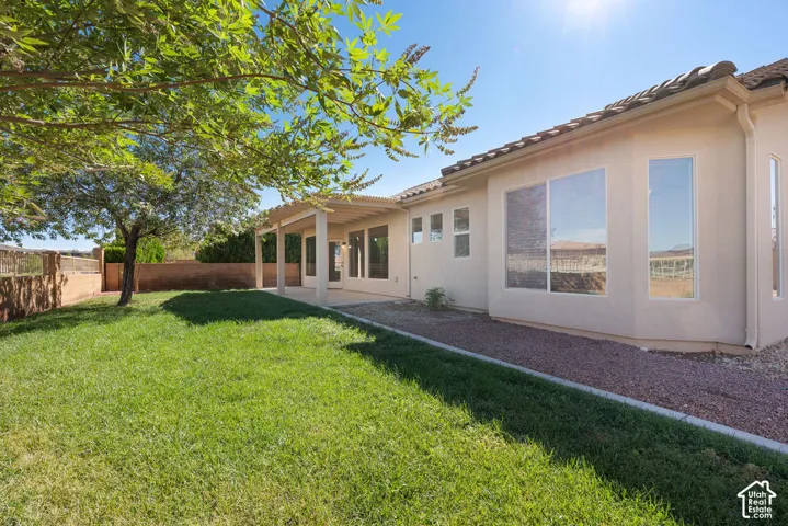 Expansive green lawn with mature tree shading, covered patio, stucco exterior, and multiple large windows
