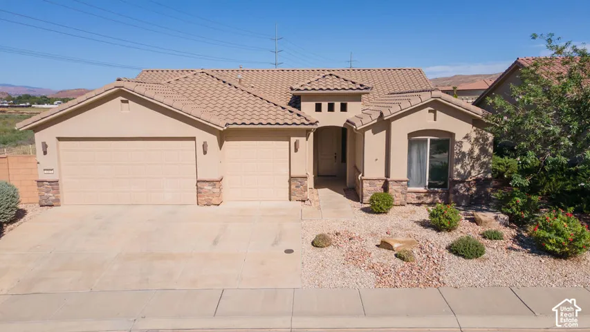 Stucco exterior with stone accents, tile roof, attached two-car garage, and desert-style landscaping