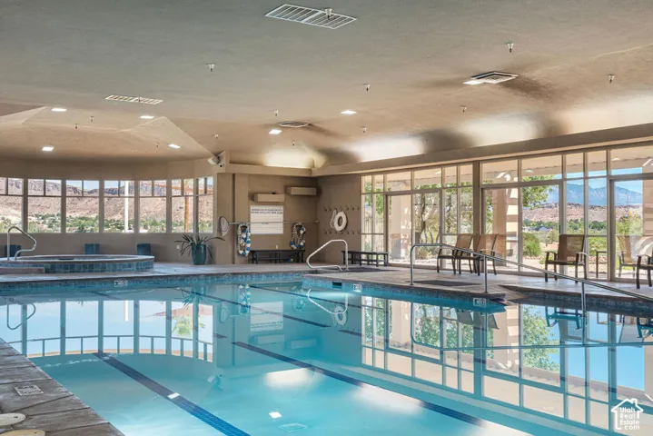 Indoor swimming pool with integrated hot tub, surrounded by expansive windows, offering natural light and distant mountain scenery
