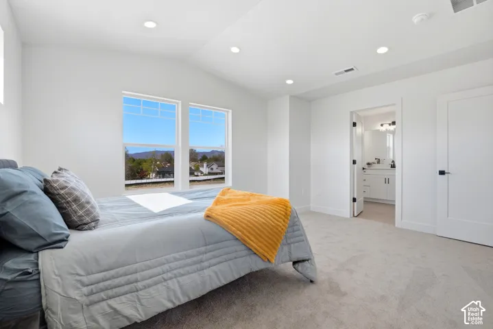 Vaulted ceilings with recessed lighting, large windows, light-toned carpeting, white interior doors with black hardware, and an en suite bathroom featuring a white vanity