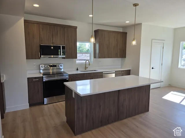 Kitchen featuring wood-finish cabinetry, stainless steel appliances, white countertops, a central island, and recessed lighting