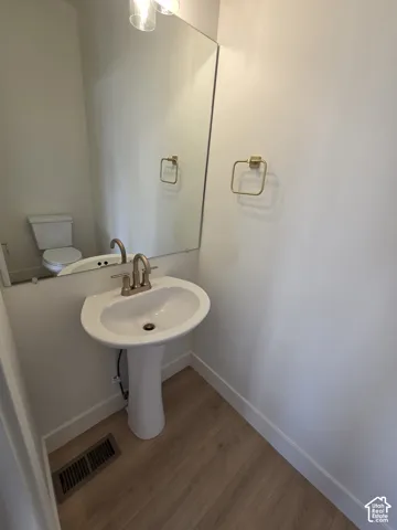 Pedestal sink with brushed nickel faucet, large wall-mounted mirror, overhead vanity lighting, and wood-finish flooring