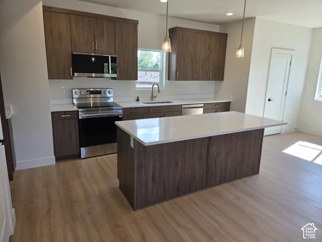 Kitchen featuring wood-finish cabinetry, stainless steel appliances, white countertops, a central island, and pendant lighting