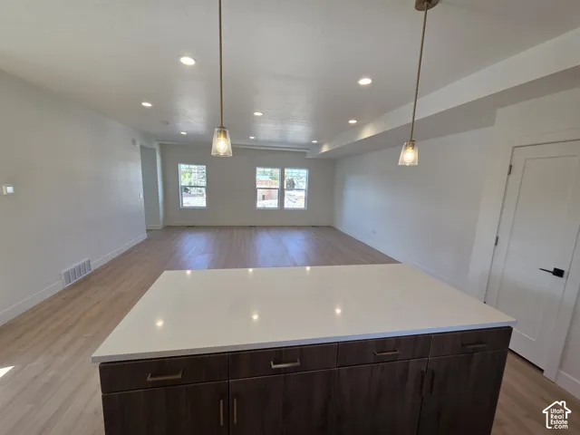 Kitchen island with a white countertop and wood-finish cabinetry, illuminated by two pendant lights and recessed lighting