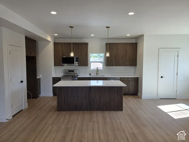 Kitchen featuring wood-finish flooring, recessed lighting, a central island with a light-colored countertop, and dark wood-tone cabinetry