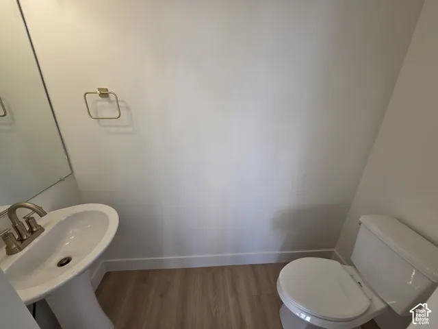 Pedestal sink with a brushed nickel faucet, large wall mirror, and wood-finish flooring