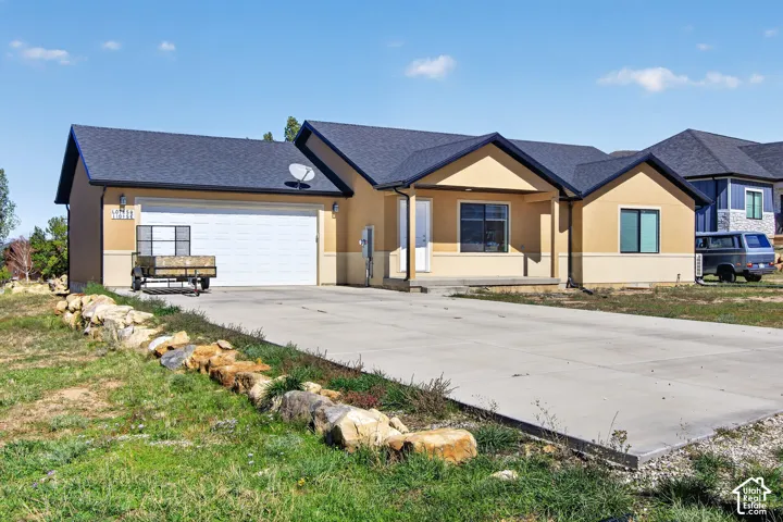 Stucco exterior with contrasting trim, black asphalt shingle roof, attached garage, and concrete driveway