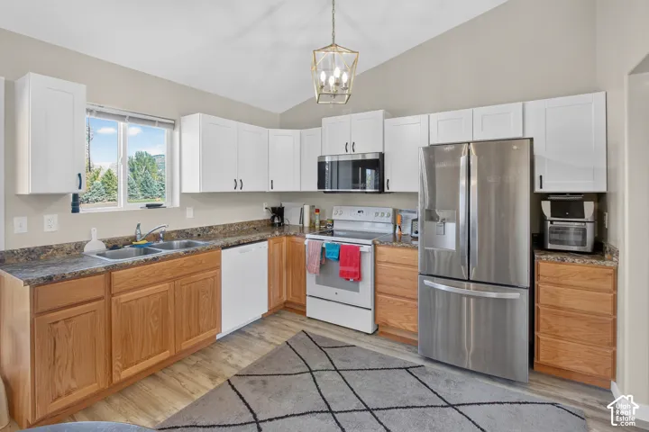Kitchen featuring white upper cabinetry, natural wood-finish lower cabinetry, wood-finish flooring, a double basin sink, and a stainless steel refrigerator