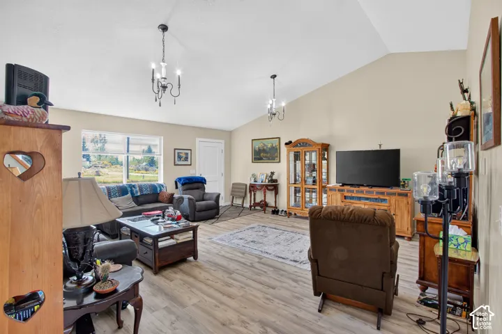 Vaulted ceiling, wood-finish flooring, multiple windows, and two chandelier light fixtures