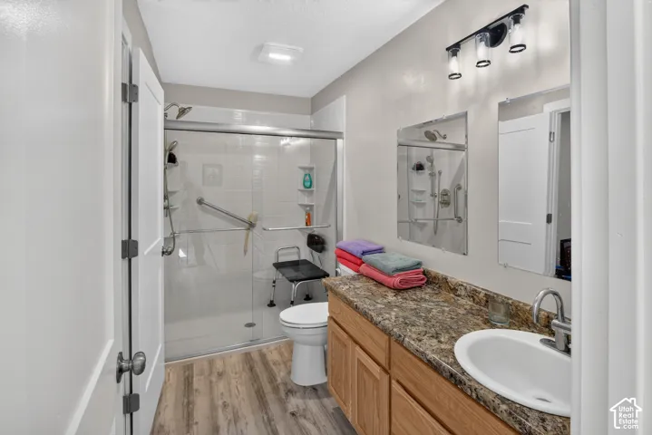 Shower with sliding glass enclosure, wood-finish flooring, vanity with a rectangular basin, and wall-mounted light fixture