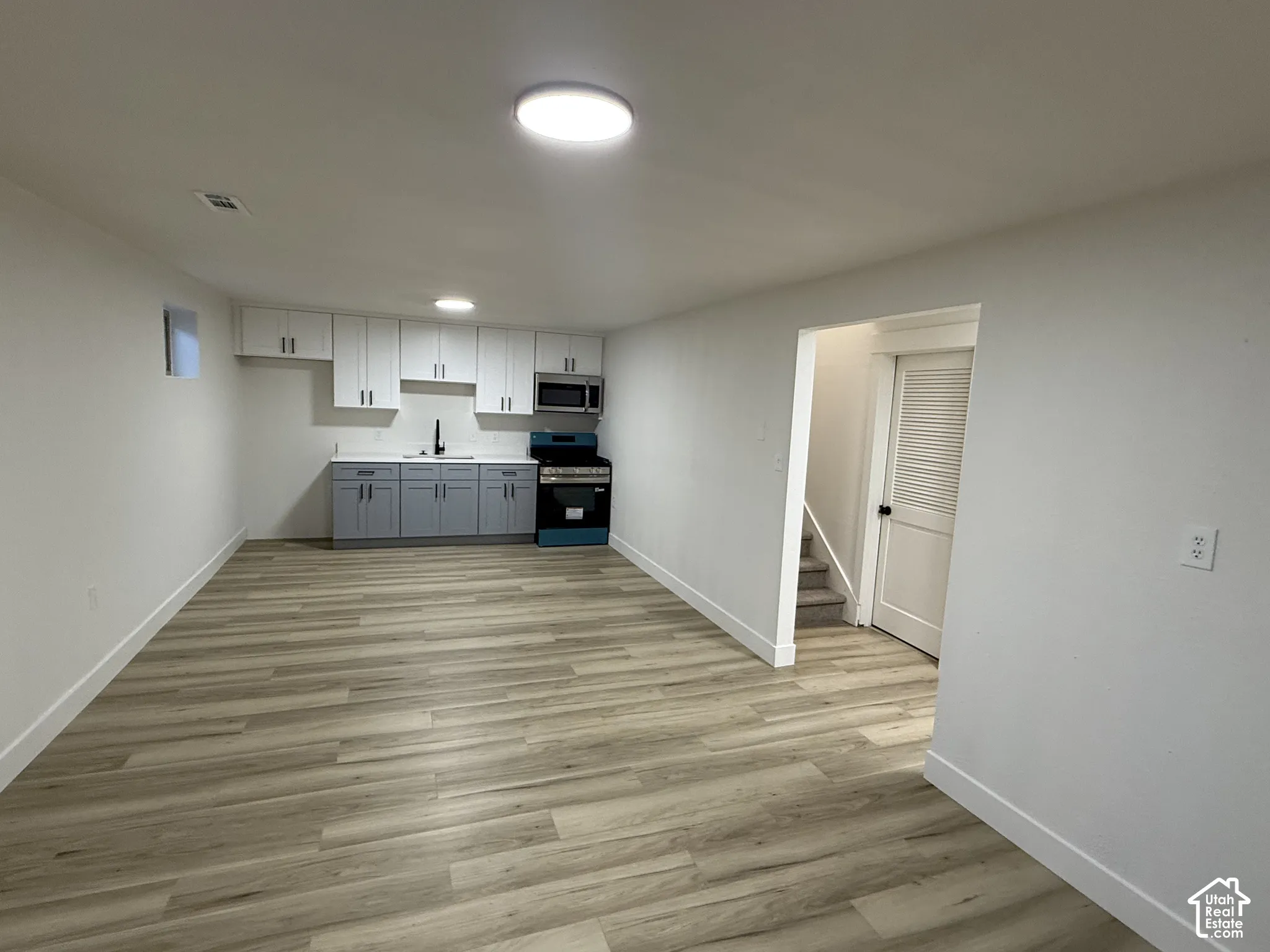 Basement kitchen with white upper cabinetry, gray lower cabinetry, and a stainless steel microwave