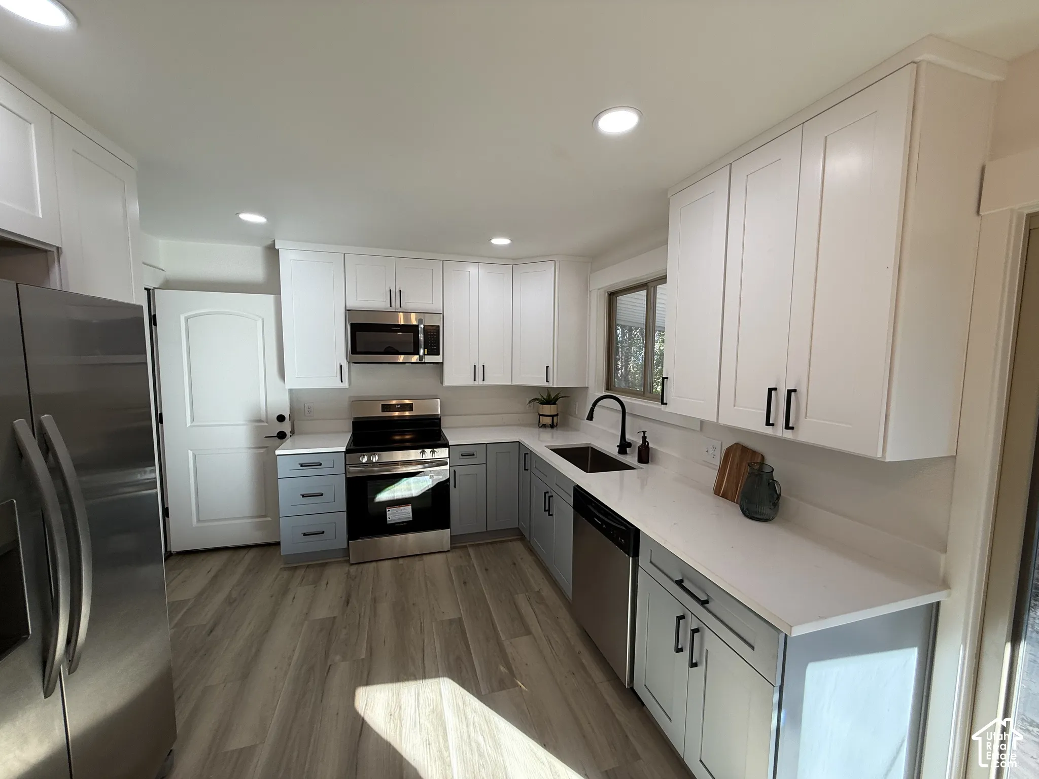 Modern kitchen featuring two-tone cabinetry, stainless steel appliances, a black matte faucet, white countertops, and wood-finish flooring